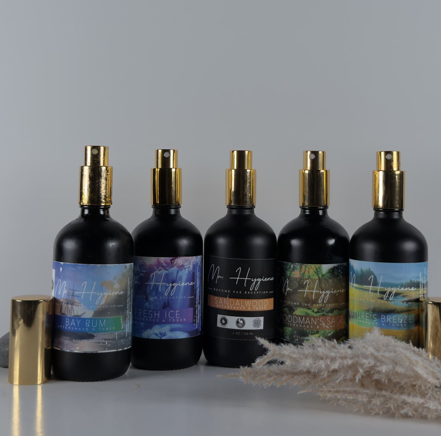 Five black spray bottles with gold nozzles on a gray background