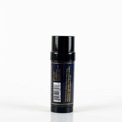 A single cosmetic stick container, shown from the back, featuring a glossy black cap and a dark navy blue body with gold text and a barcode label.